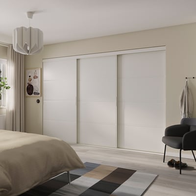 Bedroom with large white SKYTTA sliding closet doors, modern decor, beige bedding, colorful rug, and black chair.