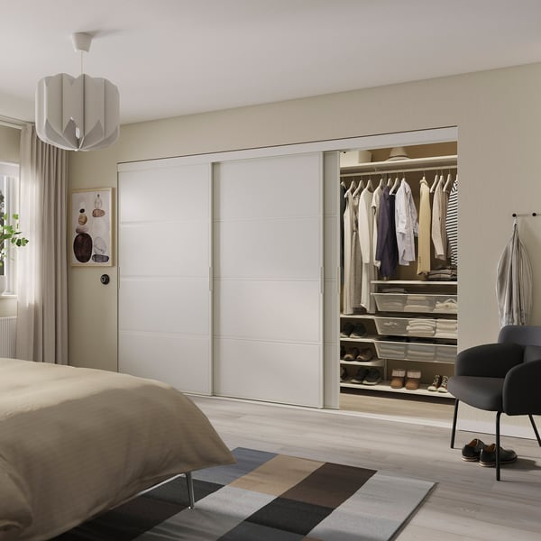 Minimalist bedroom with large SKYTTA white closet, organized clothes, and modern decor. Light-colored floor and bed.
