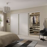 Minimalist bedroom with large SKYTTA white closet, organized clothes, and modern decor. Light-colored floor and bed.