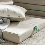 Cozy kids mattress on floor, cream-colored, soft with green handle, and decorative pillow.
