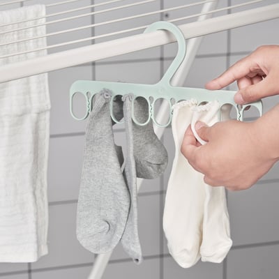 Hand hangs socks on a mint-colored hanger with multiple loops.