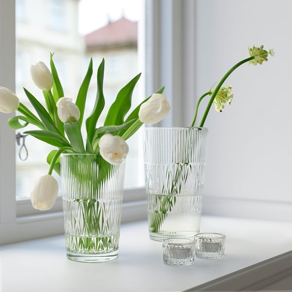 Three small, clear glass vases - two florals, one modern, arranged next to window.