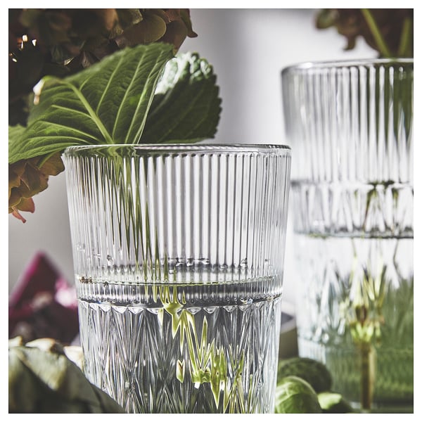Two tall, clear glass vases with vertical ribbing and a textured base, placed among green leaves.