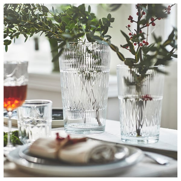Elegant table setting with the SMÄLLSPIREA glass series in clear, featuring vases with vertical patterns and flowers.