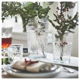 Elegant table setting with the SMÄLLSPIREA glass series in clear, featuring vases with vertical patterns and flowers.