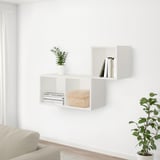 Modern living area with white walls, beige sofa, shelves with books, plant, and bamboo box. Floor plant near sofa.