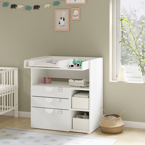 White nursery changing table with drawers, shelves, and baby items. Bright, modern design for baby care.