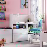 Bright pink kids room SMÅSTAD white desk and drawer set, blue chair, toy dinosaur, and wall shelves with books and toys.