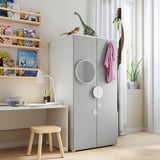 Kids room with light gray SMÅSTAD wardrobe, white desk, wood stool, lamp, books, toys, and plants.