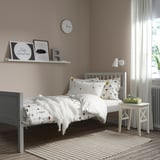 Childs bedroom with grey SMYGA bed, floral sheets, nightstand, clock shelf, and sheer curtains.