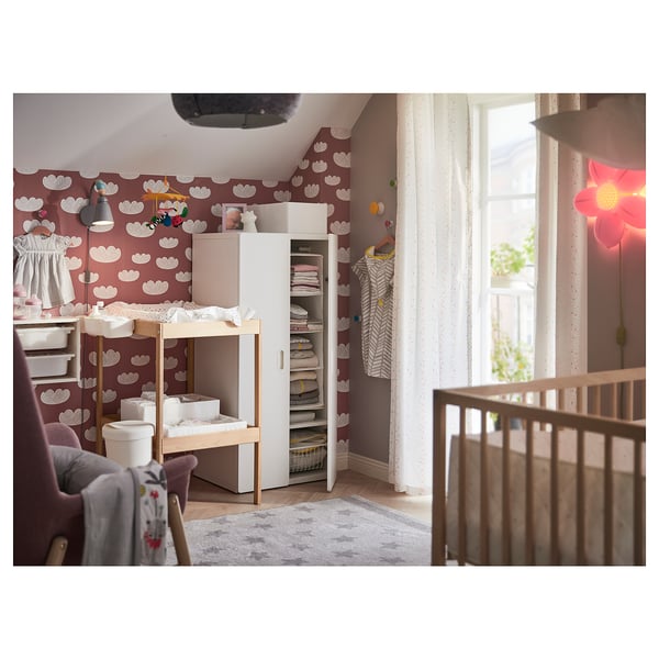 Childs room with changing table, dresser, and crib. Colorful wallpaper, lamp, and rug.