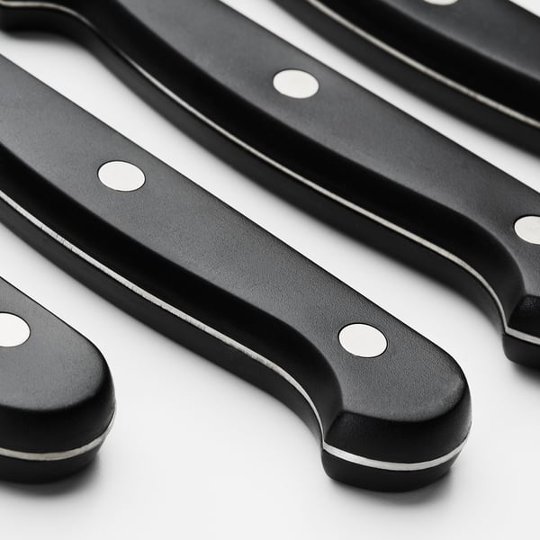 Four steak knives with black handles and serrated blades.