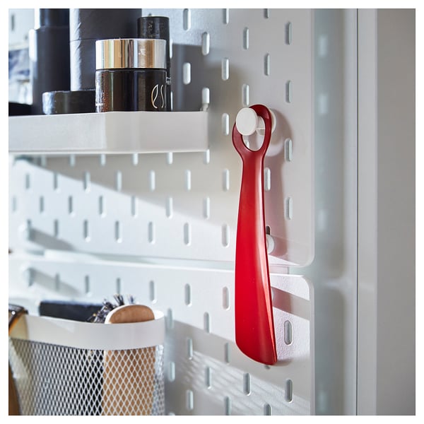 Bright red SNÖSKYFFEL shoehorn hangs on white organizer, featuring sturdy metal design.