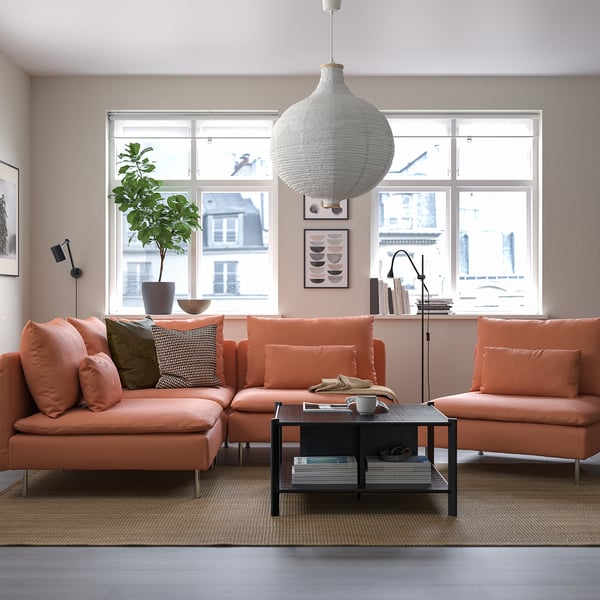 Bright orange sectional sofa in cozy living room with large window, woven pendant light, black coffee table, plant, and art.