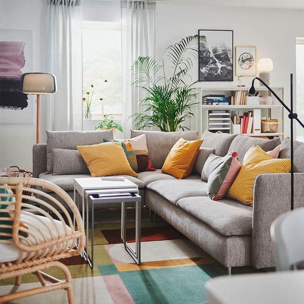 Modern living room with gray SÖDERHAMN sofa, colorful cushions, wicker chair, and plants.