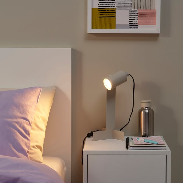 Modern bedroom with SOLHETTA lamp, yellow pillows, books, and abstract painting.