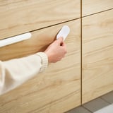 Hand pressing a white SOLSTOL nfc lock on wooden drawers.