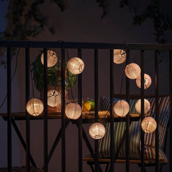 String of spherical lantern lights on balcony railing, illuminating outdoor evening space.