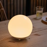 SOLVINDEN solar lamp sits on a wooden table, bright and round, near a glass and coaster. Compact yet glowing, modern design.