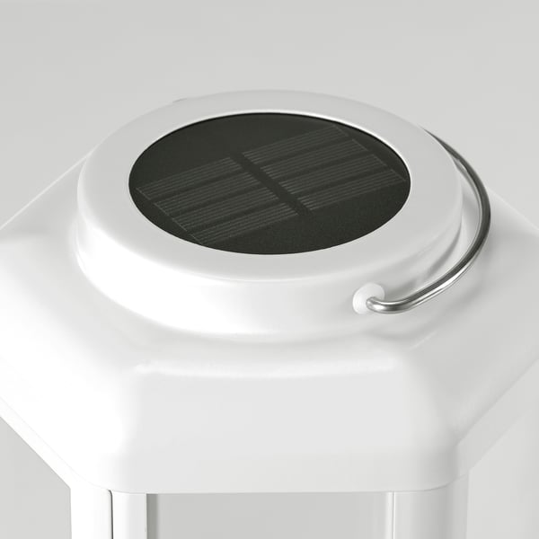 Sleek, modern solar lamp with clean lines. White body, stainless steel handle, and protective glass top. Emits warm decorative light.