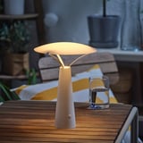 Modern table lamp on wooden table, providing warm decorative light, with glass of water nearby.
