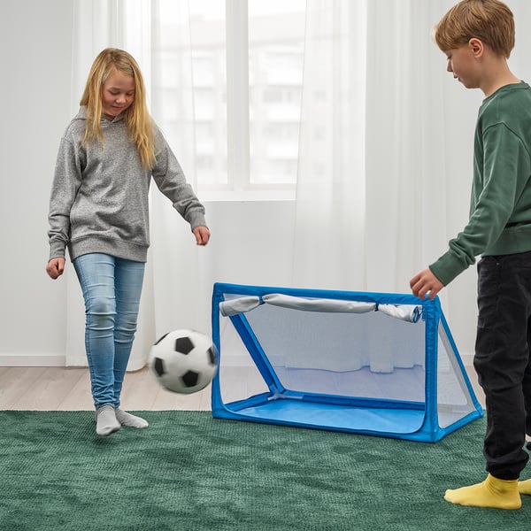 Two kids playing indoor soccer, girl kicking ball towards goal.