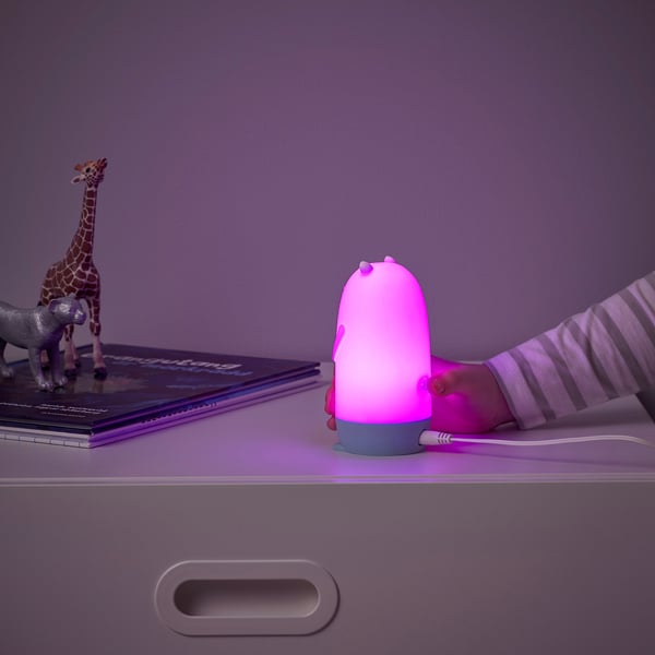 Childs hand with pink otter night light. Glows, changes colors, near toys & books.