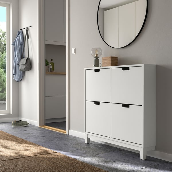 White STÄLL shoe cabinet in entryway with 4 compartments, mirror, and hooks holding coats.
