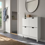 White STÄLL shoe cabinet in entryway with 4 compartments, mirror, and hooks holding coats.