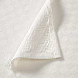 White bedspread with intricate weave pattern, folded neatly, showcasing soft, high-quality cotton texture.