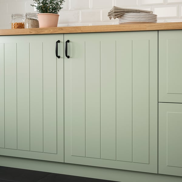 Light green kitchen cabinets with grooved panels and black handles, lacquered for stain resistance and easy cleaning.