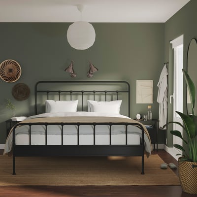 Modern bedroom with black bed, white linens, green walls, grey nightstand, art, and lights.