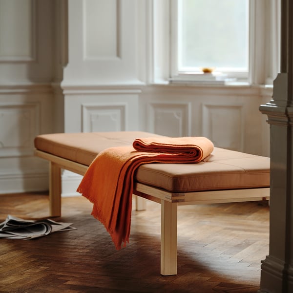This image the stockhom 2025 bench in orange leather, with a solid wood frame. Its large, well-cushioned, and sleek, modern scandinavian design.