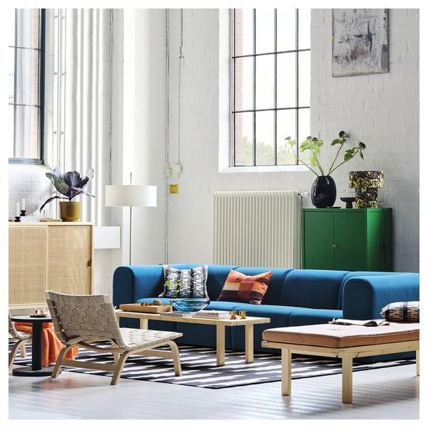 Modern living room with blue STOCKHOLM 2025 bench, light wood, rich blue leather, striped rug, wicker chair, plants. Calming, elegant atmosphere.