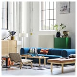 Modern living room with blue STOCKHOLM 2025 bench, light wood, rich blue leather, striped rug, wicker chair, plants. Calming, elegant atmosphere.