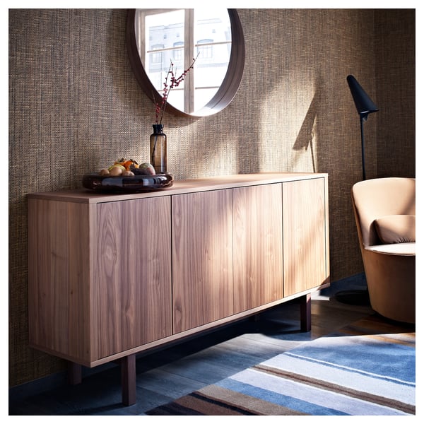 Wooden sideboard with three doors, light brown color, rectangular shape, on striped rug, near peach chair.