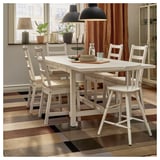 Cozy dining area with wooden table, chairs, rug, lamp, plants, and tiered tray.