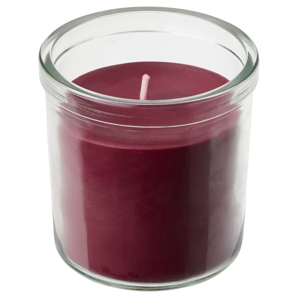 A STÖRTSKÖN candle in a clear glass. It is red-purple, cylindrical, and has a cotton wick. The candle offers a fruity, green scent.