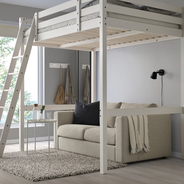 A white STORÅ loft bed with a ladder on the left, larger than surrounding furniture, featuring a sofa below.