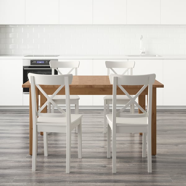 Modern kitchen with white cabinets, extendable wooden table, x-back chairs, and built-in oven.