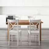 Modern kitchen with white cabinets, extendable wooden table, x-back chairs, and built-in oven.