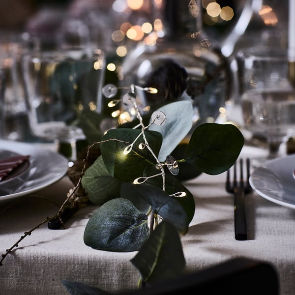 Holiday table with silver light chain, green leaves, plates, and cutlery.
