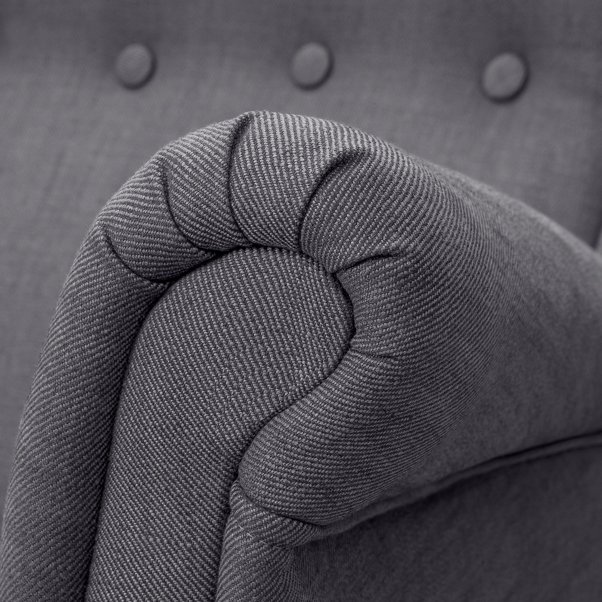 Close-up of high-quality, gray tweed fabric on a upholstered sofa armrest, showcasing its texture and detail.