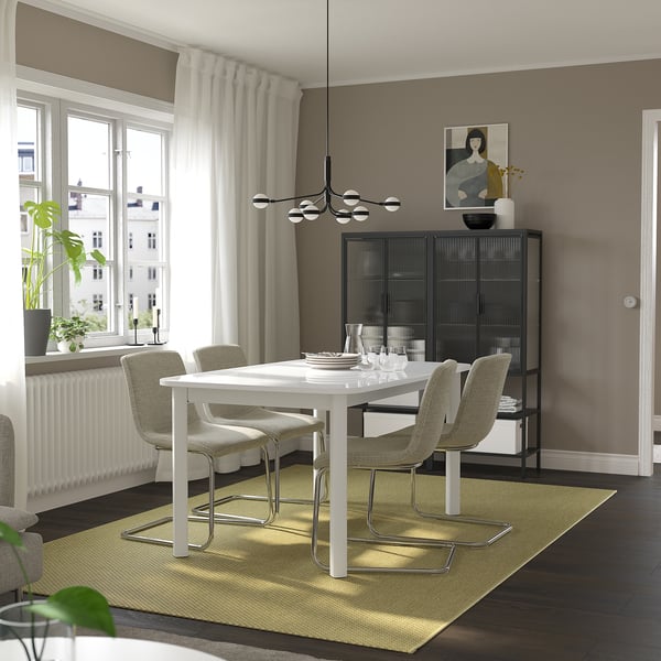 Modern dining room with white STRANDTORP extendable table, grey chairs, glass cabinet, and green rug. Large window for natural light.