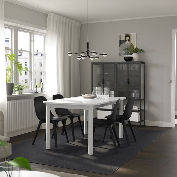 Modern dining room with extendable table, black chairs, large window, gray walls.