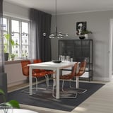 Modern dining with white STRANDTORP table and brown chairs, metal-framed, grey curtains, black bookshelf.