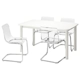 A white STRANDTORP extendable table with four clear plastic chairs, featuring chrome frames. The table and chairs have modern, sleek designs.