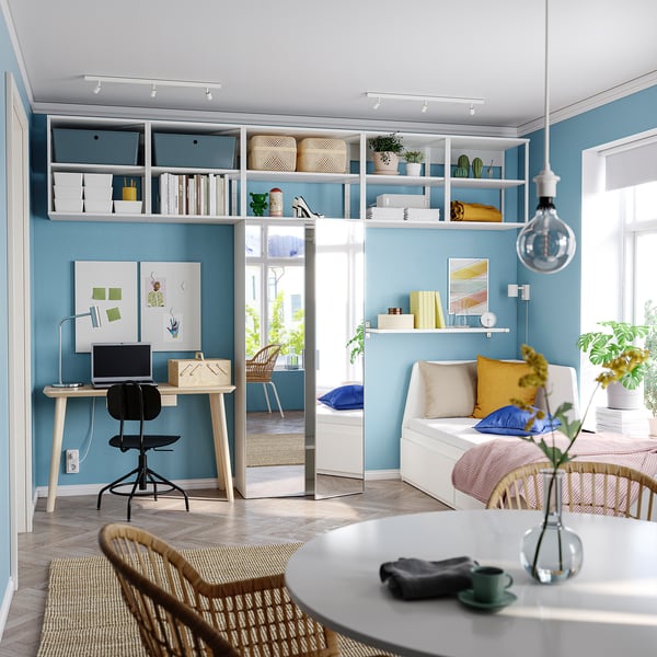 Modern home office with wooden desk, black chair, and bookshelves, featuring a blue accent wall and a mirror door.