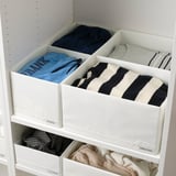 White storage shelves with labeled boxes holding neatly folded clothes, showcasing organized storage for different types of garments.