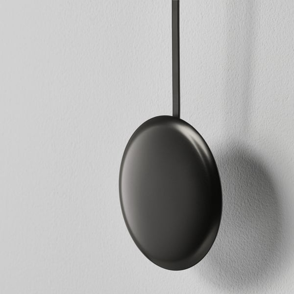 Modern black oval pendant light hangs vertically from ceiling, emitting sleek minimalist design.
